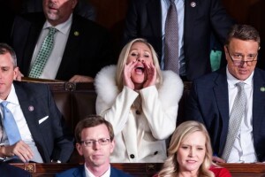Wearing a fashionable white dress with fur collar, Representative Marjorie Taylor Green (R-Georgia) stands and cups her hands around her mouth like a megaphone as she jeers President Joe Biden at the 2023 State of the Union address at the U.S. Capitol.