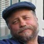 The photo is a headshot of Mark Willis, author and publisher of this web site. It was taken in Paris in 2007 by JoAnn. He is bearded and wears a blue flat cap. His beard is not as gray as it is today.