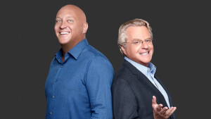 Steve “the Bouncer” Wilk0s (left) and Jerry Springer. The men stand back-to-back and turn their heads to look at the camera. Bald, taller and stockier than Springer, Steve the Bouncer is dressed informally in a blue open-collar shirt. Bespectacled with graying hair, Jerry wears a suit jacket, customary garb of a TV host. He extends his right arm toward the camera in a gesture of welcome. [Via Entertainment Tonight 042723]